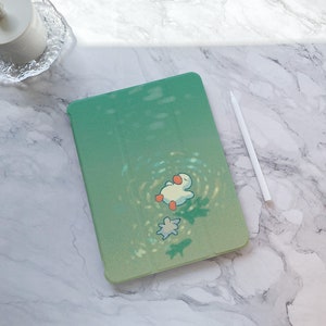 Puede incluir: Una funda verde para iPad con una ilustración de un pato blanco flotando en un círculo de luz. La funda tiene un degradado sutil de un verde más oscuro a un verde más claro.