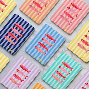 May include: A collection of colorful, striped rectangular items, each featuring a pattern of three red and pink fish. The items have different background colors, including blue, pink, yellow, and green, with names printed on them.