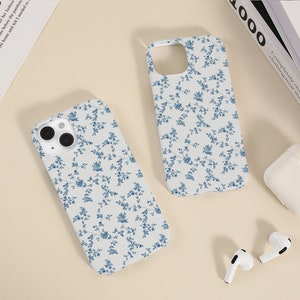 May include: Two white iPhone cases with a blue floral pattern. The cases are on a white surface.