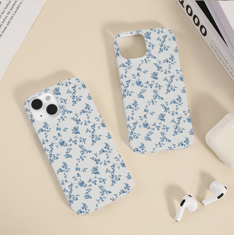 May include: Two white iPhone cases with a blue floral pattern. The cases are on a white surface.