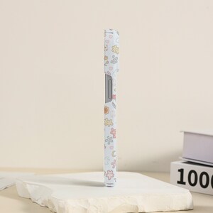 May include: A white phone case with a floral pattern in pastel colors. The pattern includes flowers, hearts, stars, and moons.