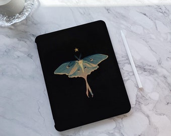 May include: Black tablet case featuring a detailed illustration of a Luna moth with teal and yellow wings, and a small gold star above it. The moth design is centered on the case. A white stylus is next to the case on a marble surface.