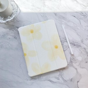 Könnte beinhalten: Eine weiße Tablethülle mit Blumenmuster. Die Hülle hat ein dezentes gelbes Blumenmuster auf weißem Hintergrund.