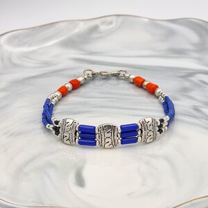May include: A multi-strand bracelet featuring blue and orange beads with silver accents. The bracelet has a silver clasp.
