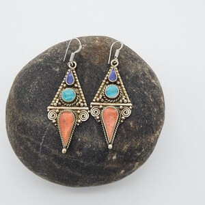 May include: A pair of silver dangle earrings with a triangular design. The earrings feature turquoise and lapis lazuli stones set in a gold-toned metal.