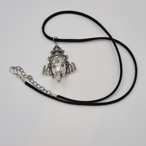Op de afbeelding: Een zilveren ketting met een hanger met het gezicht van de hindoe&iuml;stische god Ganesha. De hanger is bevestigd aan een zwart koord.
