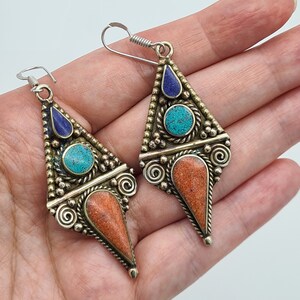 May include: A pair of silver dangle earrings with turquoise and lapis lazuli stones set in a triangular design.