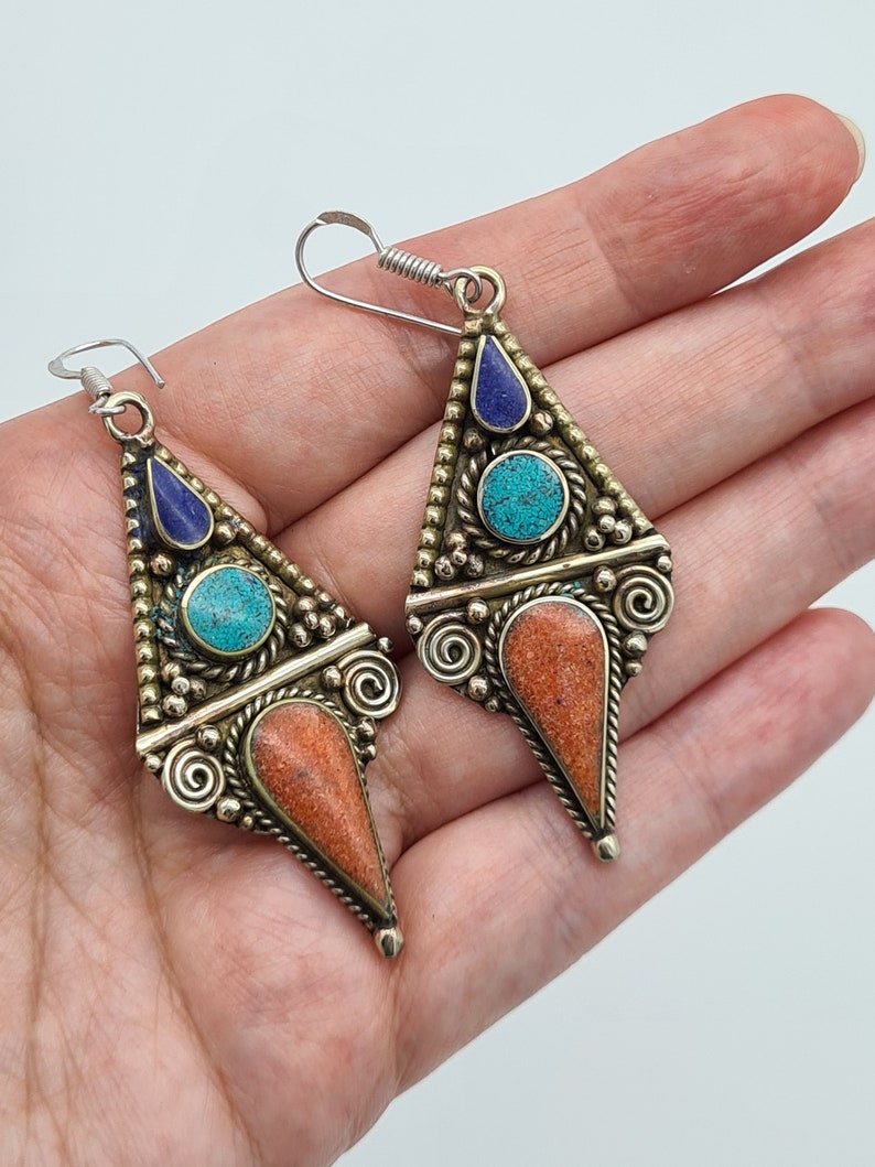 May include: A pair of silver dangle earrings with turquoise and lapis lazuli stones set in a triangular design.