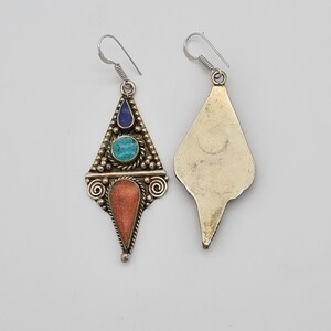 May include: A pair of dangle earrings with a geometric design. The earrings are made of metal and feature turquoise, coral, and lapis lazuli stones.