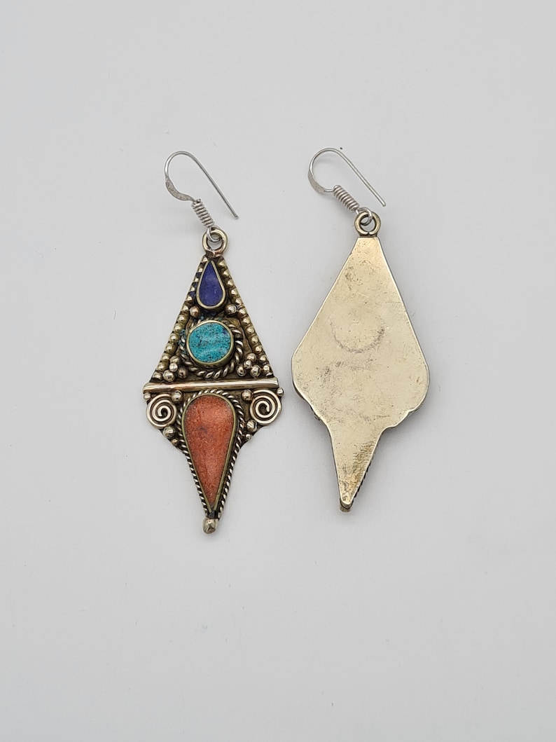 May include: A pair of dangle earrings with a geometric design. The earrings are made of metal and feature turquoise, coral, and lapis lazuli stones.