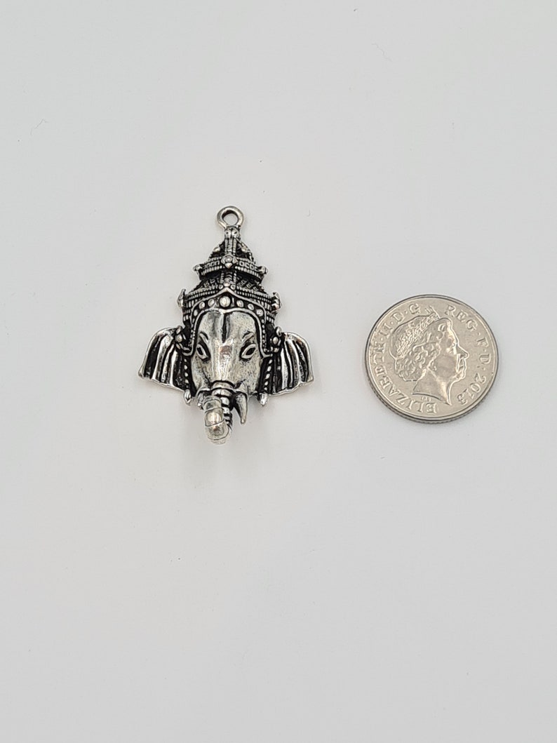 Op de afbeelding: Zilveren bedelhanger met een gedetailleerde afbeelding van de hindoe-god Ganesha, met een kroon en een olifantenkop. De bedel wordt getoond naast een Britse munt van &eacute;&eacute;n pond ter vergelijking van de grootte.
