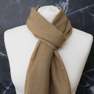 May include: A brown scarf made of soft fabric. The scarf is folded and draped around a mannequin's neck.