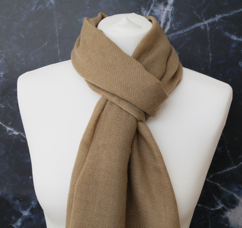 May include: A brown scarf made of soft fabric. The scarf is folded and draped around a mannequin's neck.