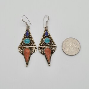 May include: A pair of dangle earrings with a triangular design. The earrings are made of silver and feature turquoise and lapis lazuli stones.