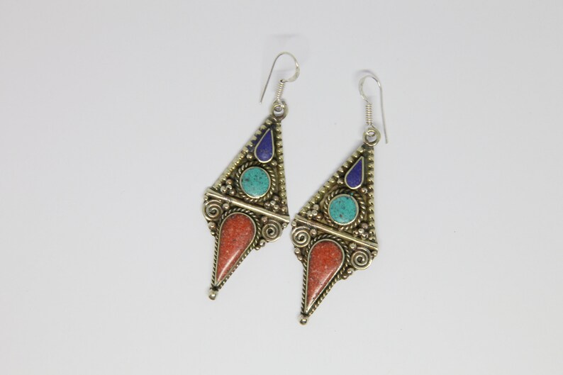 May include: A pair of silver dangle earrings with turquoise, coral, and lapis lazuli stones. The earrings are in the shape of a triangle with a pointed bottom.