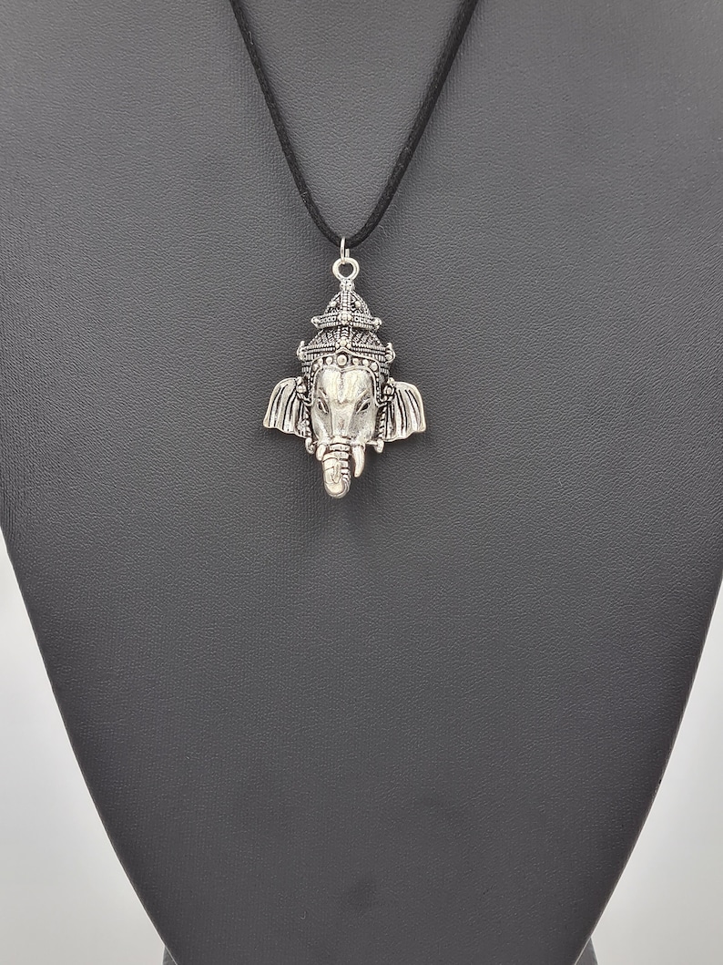 Op de afbeelding: Een zilveren ketting met een gedetailleerde hanger die de hindoe-god Ganesha voorstelt. De ketting heeft een zwart koord.