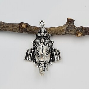 Op de afbeelding: Zilveren bedelhanger met een gedetailleerde afbeelding van de hindoe&iuml;stische godheid Ganesha, de olifantenkopgod van wijsheid en geluk. De bedel heeft een getextureerd, versierd ontwerp en is perfect voor het maken van sieraden of knutselen.
