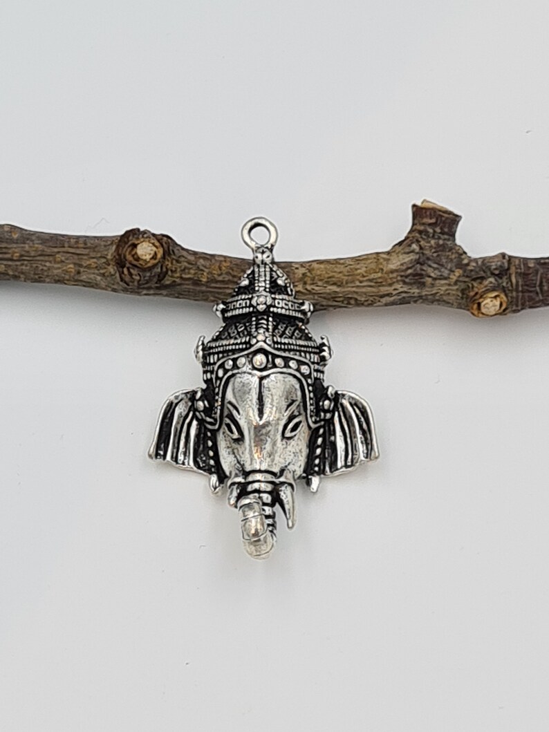 Op de afbeelding: Zilveren bedelhanger met een gedetailleerde afbeelding van de hindoe&iuml;stische godheid Ganesha, de olifantenkopgod van wijsheid en geluk. De bedel heeft een getextureerd, versierd ontwerp en is perfect voor het maken van sieraden of knutselen.