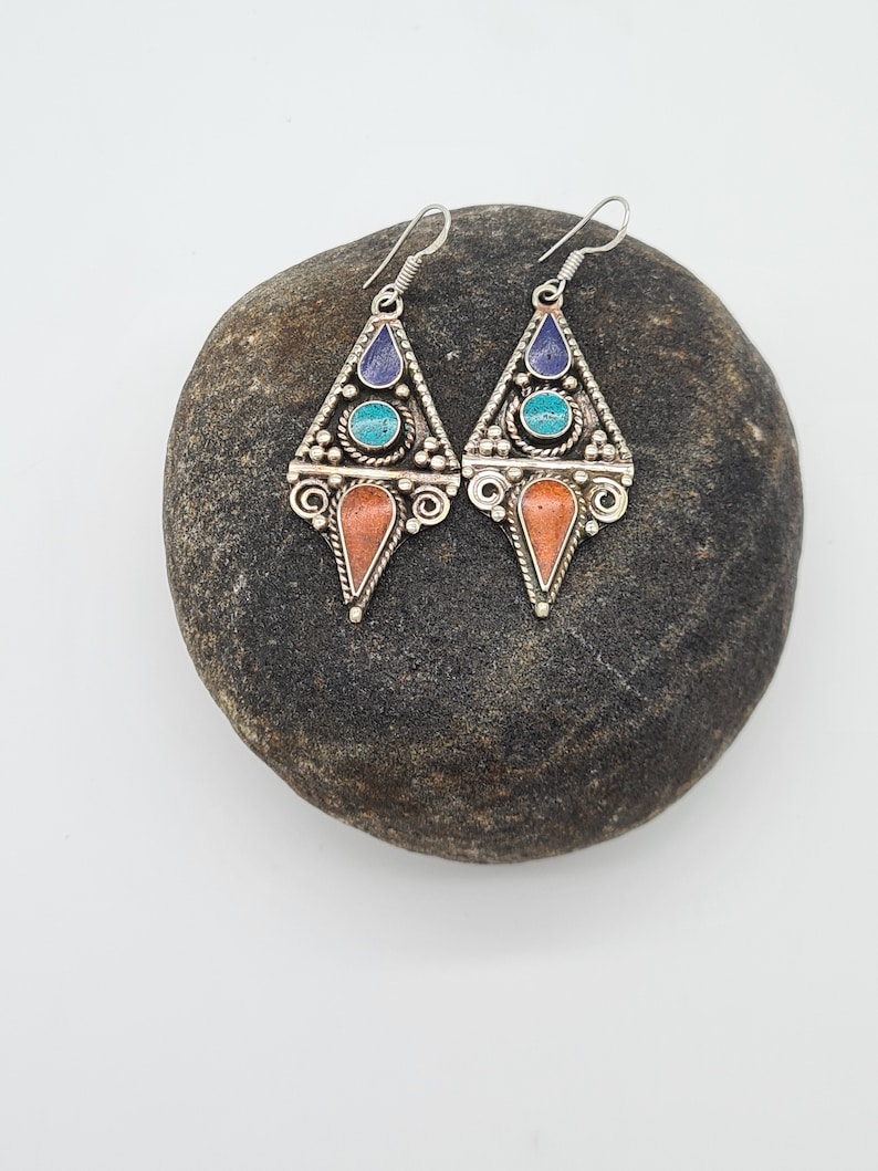 May include: A pair of silver dangle earrings with turquoise, coral, and lapis lazuli stones. The earrings are in the shape of a triangle with intricate details.