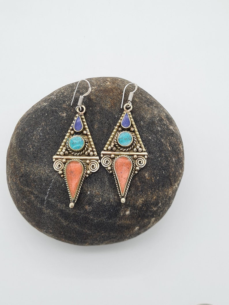 May include: A pair of silver dangle earrings with a triangular design. The earrings feature turquoise and lapis lazuli stones set in a gold-toned metal.