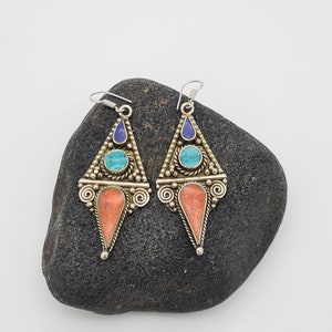May include: A pair of silver dangle earrings with turquoise, coral, and lapis lazuli stones. The earrings are in the shape of a triangle with a pointed bottom.