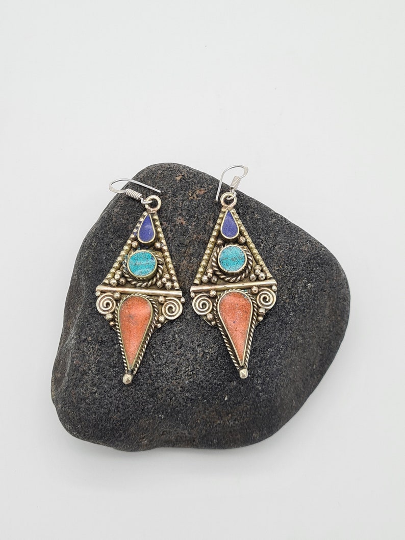 May include: A pair of silver dangle earrings with turquoise, coral, and lapis lazuli stones. The earrings are in the shape of a triangle with a pointed bottom.