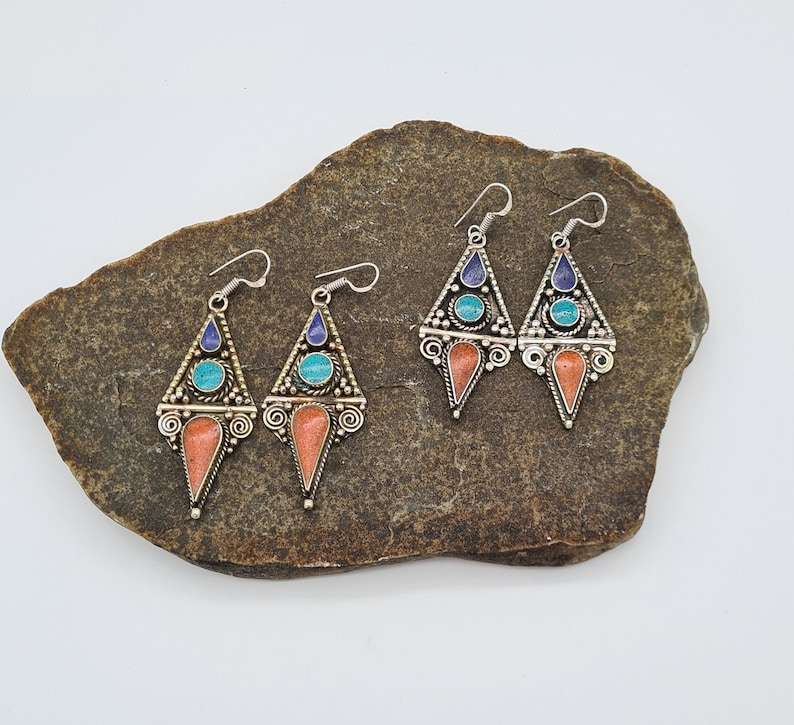 May include: Four silver dangle earrings with turquoise and blue stones and coral accents. The earrings are displayed on a brown rock.