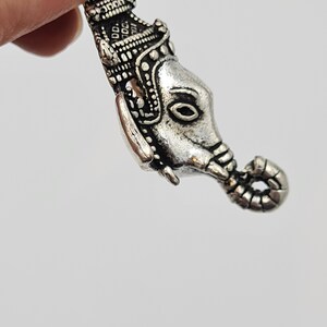 Op de afbeelding: Zilveren bedel met een gedetailleerd olifantenhoofd met een kroon erop. De slurf van de olifant is opgerold en de bedel heeft een lus om aan een armband of ketting te bevestigen.