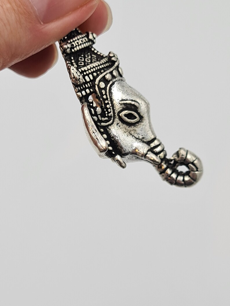 Op de afbeelding: Zilveren bedel met een gedetailleerd olifantenhoofd met een kroon erop. De slurf van de olifant is opgerold en de bedel heeft een lus om aan een armband of ketting te bevestigen.