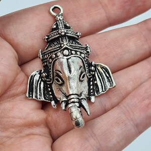 Op de afbeelding: Zilveren hanger met een gedetailleerde afbeelding van de hindoe-god Ganesha, met een kroon en een olifantenkop.