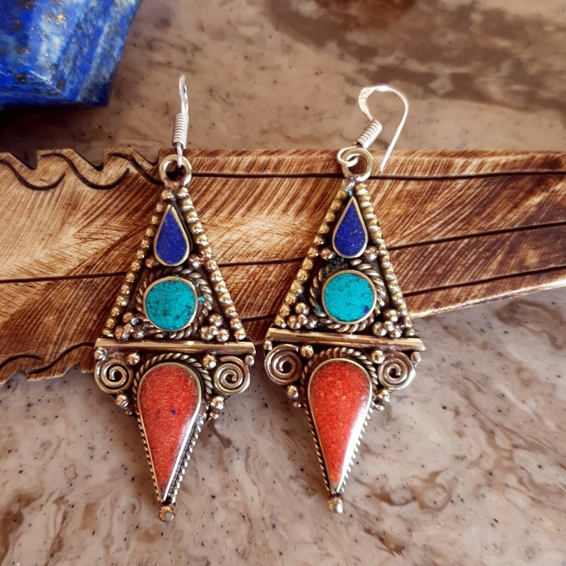 May include: A pair of silver dangle earrings with a triangular design. The earrings feature blue lapis lazuli, turquoise, and coral stones.
