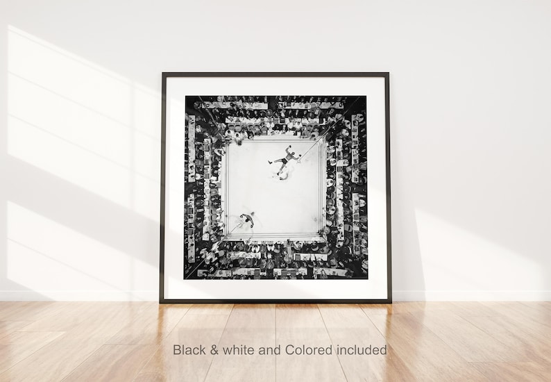 May include: Black and white framed print of a boxing match, viewed from above. Two boxers are in the ring, surrounded by a crowd. The print is displayed on a white wall with a wooden floor. Text at the bottom reads "Black & white and Colored included."