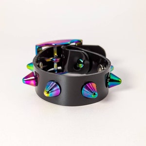 Peut inclure: Un bracelet en cuir noir avec des pointes métalliques irisées. Le bracelet a une fermeture à boucle.
