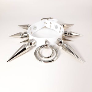 May include: White leather choker with silver spikes and a double ring pendant.