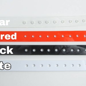 May include: Four plastic wristbands in different colors: clear, clear red, black, and white. Each wristband has multiple holes for adjustment.