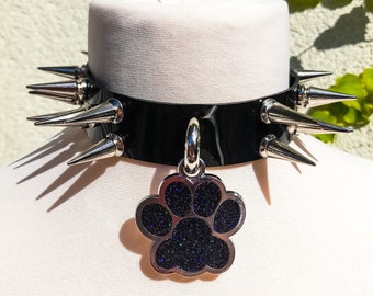 May include: Black leather choker collar with silver spikes and a silver paw print charm. The charm is covered in black glitter.