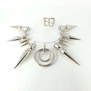 May include: A clear plastic choker necklace with silver metal spikes and a double ring pendant.
