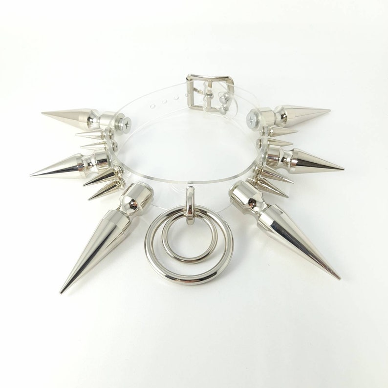 May include: A clear plastic choker necklace with silver metal spikes and a double ring pendant.