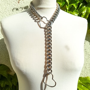 Op de afbeelding: Een zilveren ketting met twee grote hartvormige bedels. De ketting is dik en stevig, en de harten zijn open en hol.