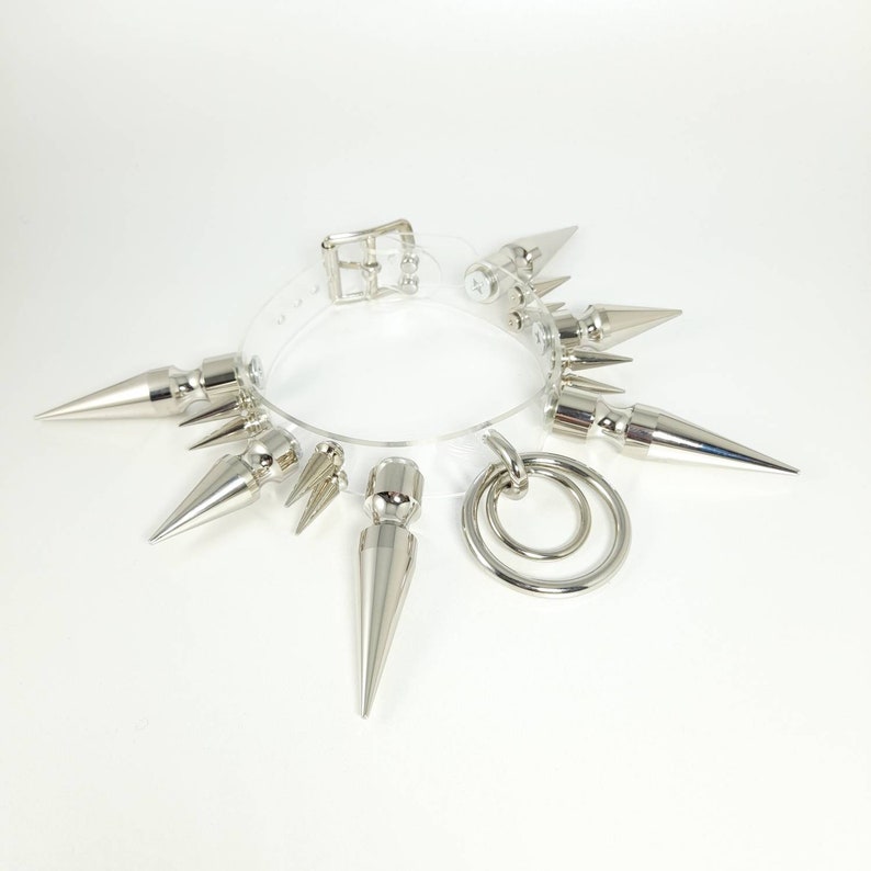 May include: A clear plastic choker with silver spikes and a silver ring attached. The choker is a fashion accessory.