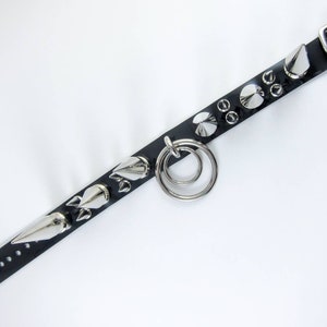 May include: Black leather bracelet with silver spikes and a double ring. The bracelet has a buckle closure.