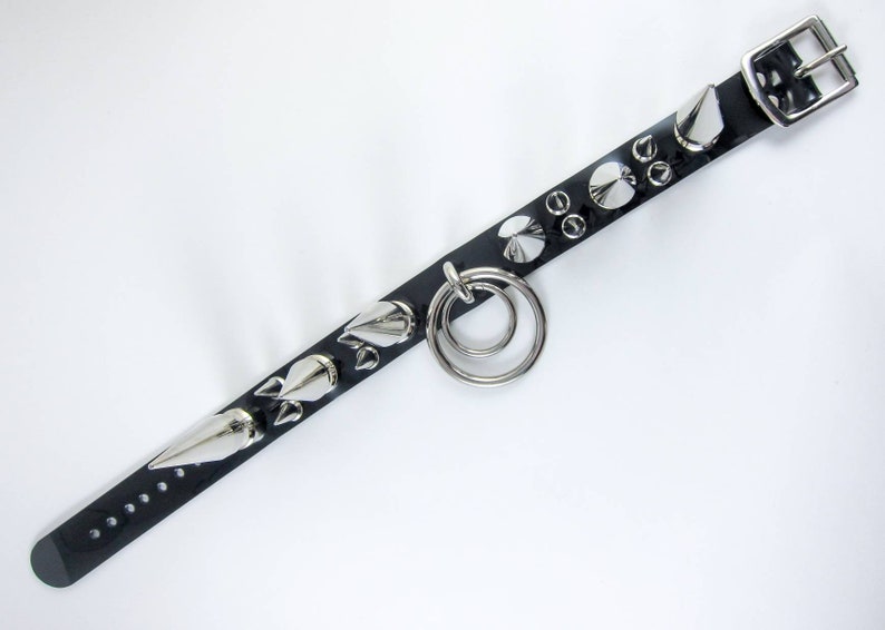 May include: Black leather bracelet with silver spikes and a double ring. The bracelet has a buckle closure.