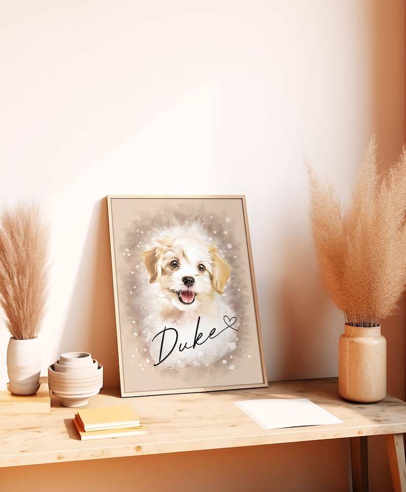 May include: A framed portrait of a happy, light-colored dog named Duke. The artwork features a watercolor-style background with the dog's name in cursive and a small heart. The frame is a light gold color, and the portrait is leaning against a wall.