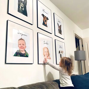 May include: Gallery wall featuring framed portraits of pets and children. Each portrait is in a black frame with a white mat. The portraits include a dog named Moose, a child named Grayson, a dog named Jake, a child named Sadie, a dog named Ellie, and another dog.