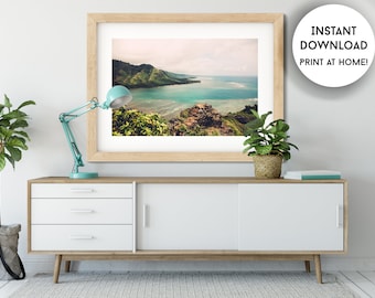May include: A framed landscape print featuring a coastal view with turquoise water, green hills, and a cloudy sky. The print is displayed on a white and wood-toned cabinet, with a teal desk lamp and potted plants. Text on the right says "INSTANT DOWNLOAD PRINT AT HOME!"