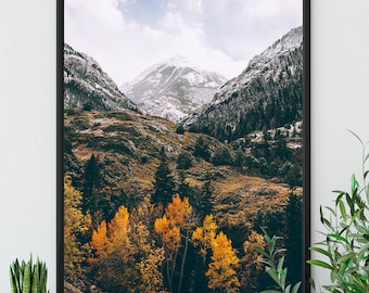 Puede incluir: Fotografía enmarcada de un paisaje montañoso. La imagen presenta picos nevados, árboles de hoja perenne y vibrante follaje otoñal amarillo. El cielo es una mezcla de nubes azules y blancas.
