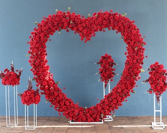 May include: A heart-shaped floral arrangement made of red roses, perfect for a wedding or special event. The roses are arranged on a white metal stand.