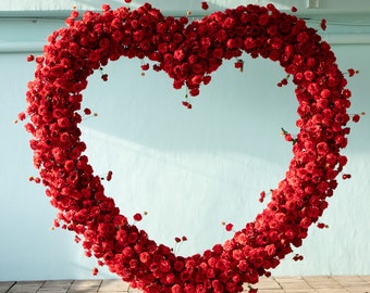 May include: A heart-shaped floral arch made of red roses. The arch is standing on a wooden floor.