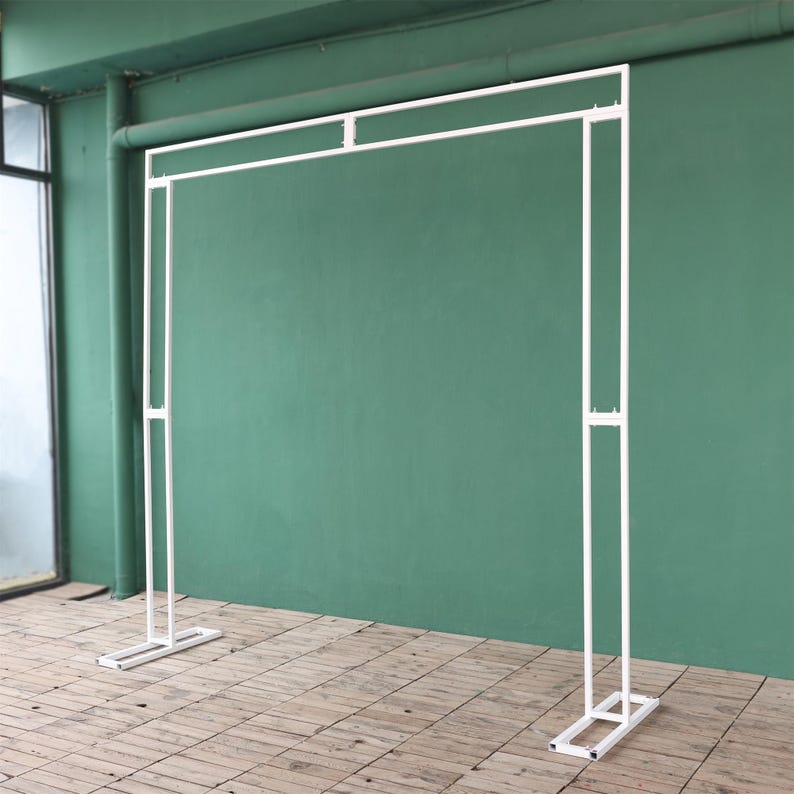 May include: White metal archway backdrop for a wedding or event. The archway is freestanding and has a simple, modern design.
