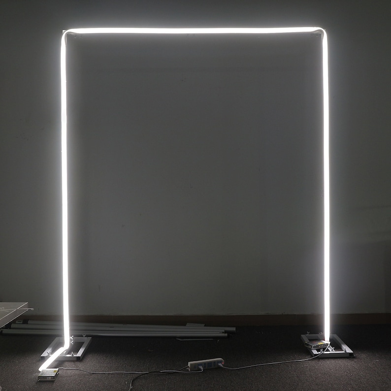 K&ouml;nnte beinhalten: Ein wei&szlig;er LED-Lichtrahmen, der auf einem schwarzen Boden steht, mit einem Stromkabel, das in eine Steckdose gesteckt ist.
